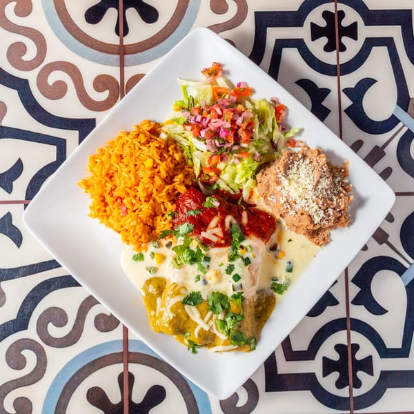 Mexican-style platter with orange rice, enchiladas, crispy chicken, salad, colorful salsa, and creamy sauce on patterned tiles.