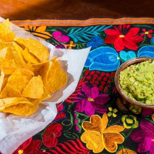 A basket of tortilla chips and a bowl of guacamole on a colorful floral tablecloth.