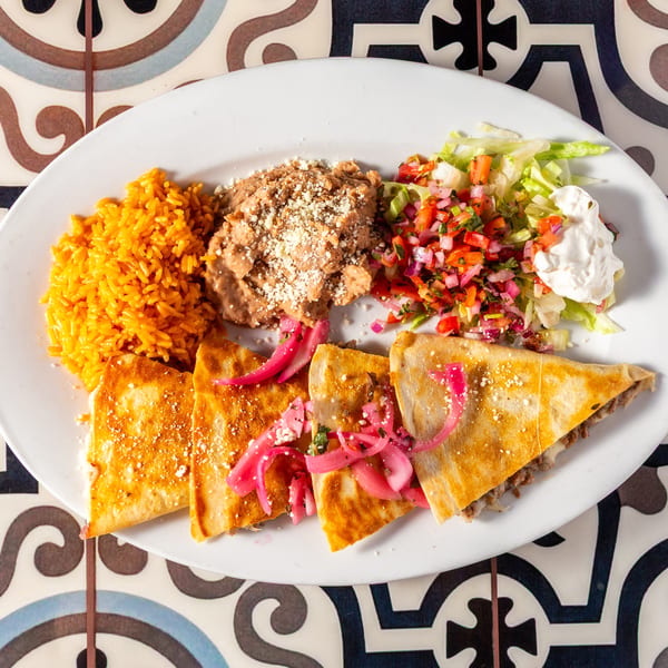 Large platter of golden rice, cheesy fried chicken, quesadillas, salad, pico de gallo, pickled onions, and sour cream.