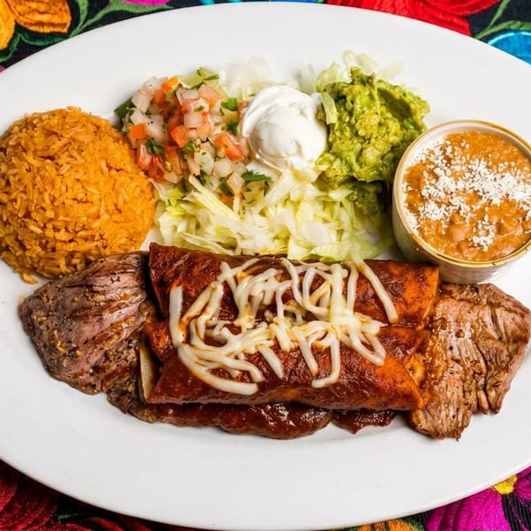 Mexican platter with enchiladas, steak, rice, beans, guacamole, pico de gallo, and sour cream.