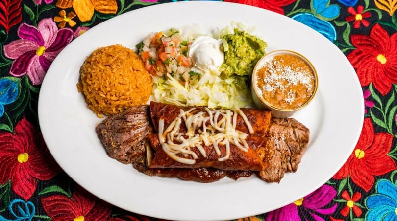 Mexican platter with enchiladas, steak, rice, beans, guacamole, pico de gallo, and sour cream.
